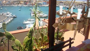 Un balcon donnant sur une marina, agrémenté de plantes en pot et d’un luminaire en métal au style rustique.