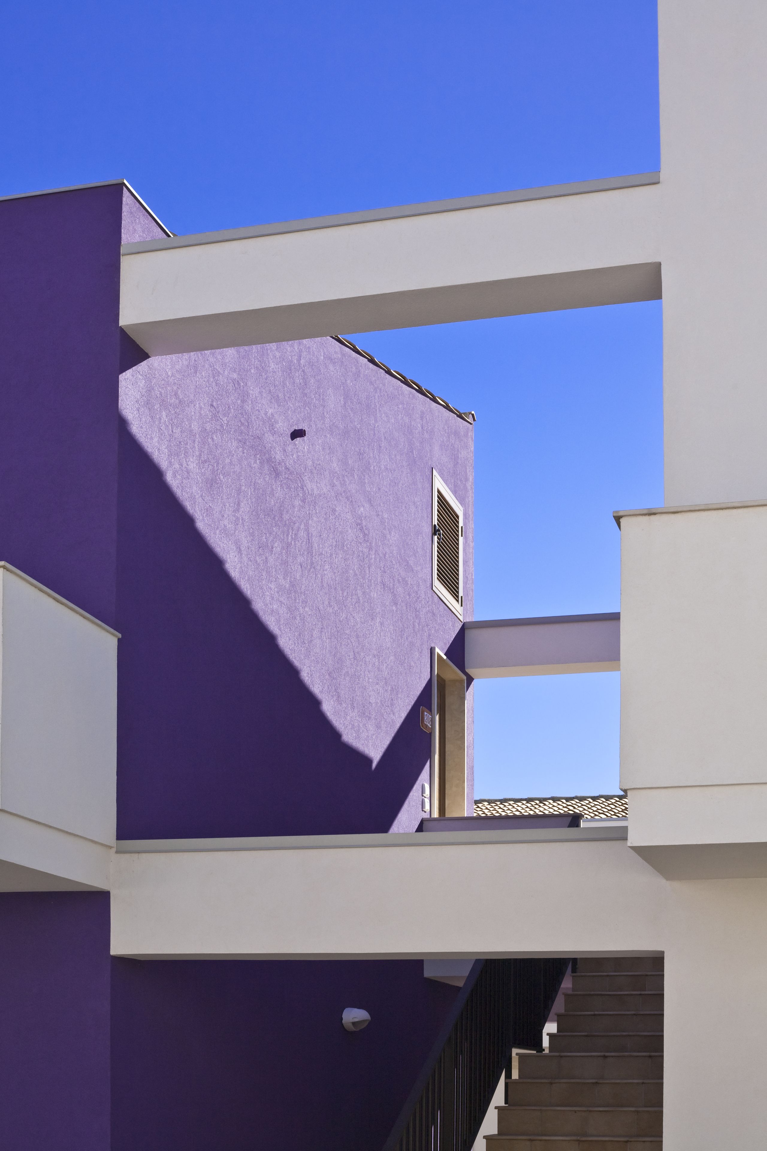 Um edifício com vários níveis, fachada roxa e partes superiores brancas.