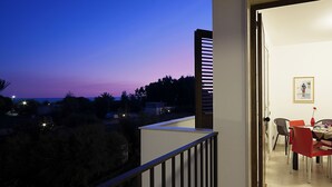 A balcony with a view of the sunset, a dining area with red chairs, and a framed picture on the wall. - Residence Blu ModicAmare (Modica)