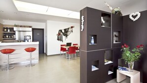 A modern kitchen with a bar area, red bar stools, and a dining table with chairs. - Residence Blu ModicAmare (Modica)