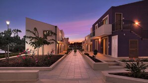 A pathway leading to a row of modern buildings with balconies and a well-maintained garden with pink flowers. - Residence Blu ModicAmare (Modica)