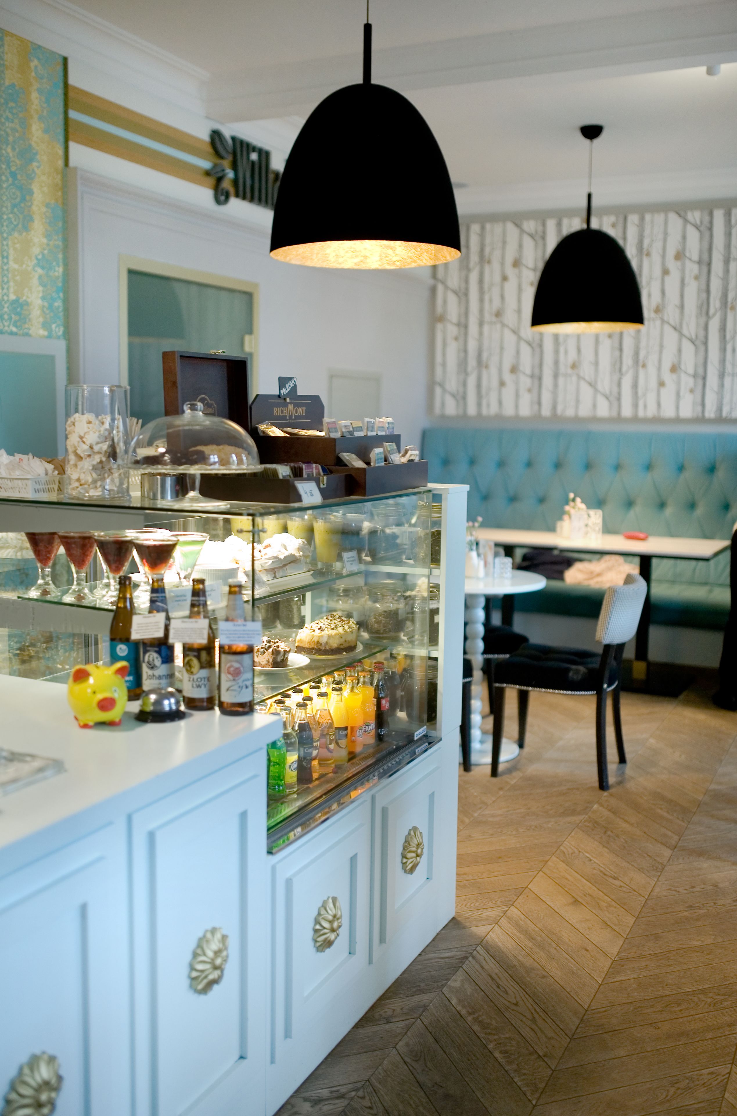 A restaurant with a glass display case filled with desserts and beverages, a blue cushioned booth, and a wooden herringbone floor.