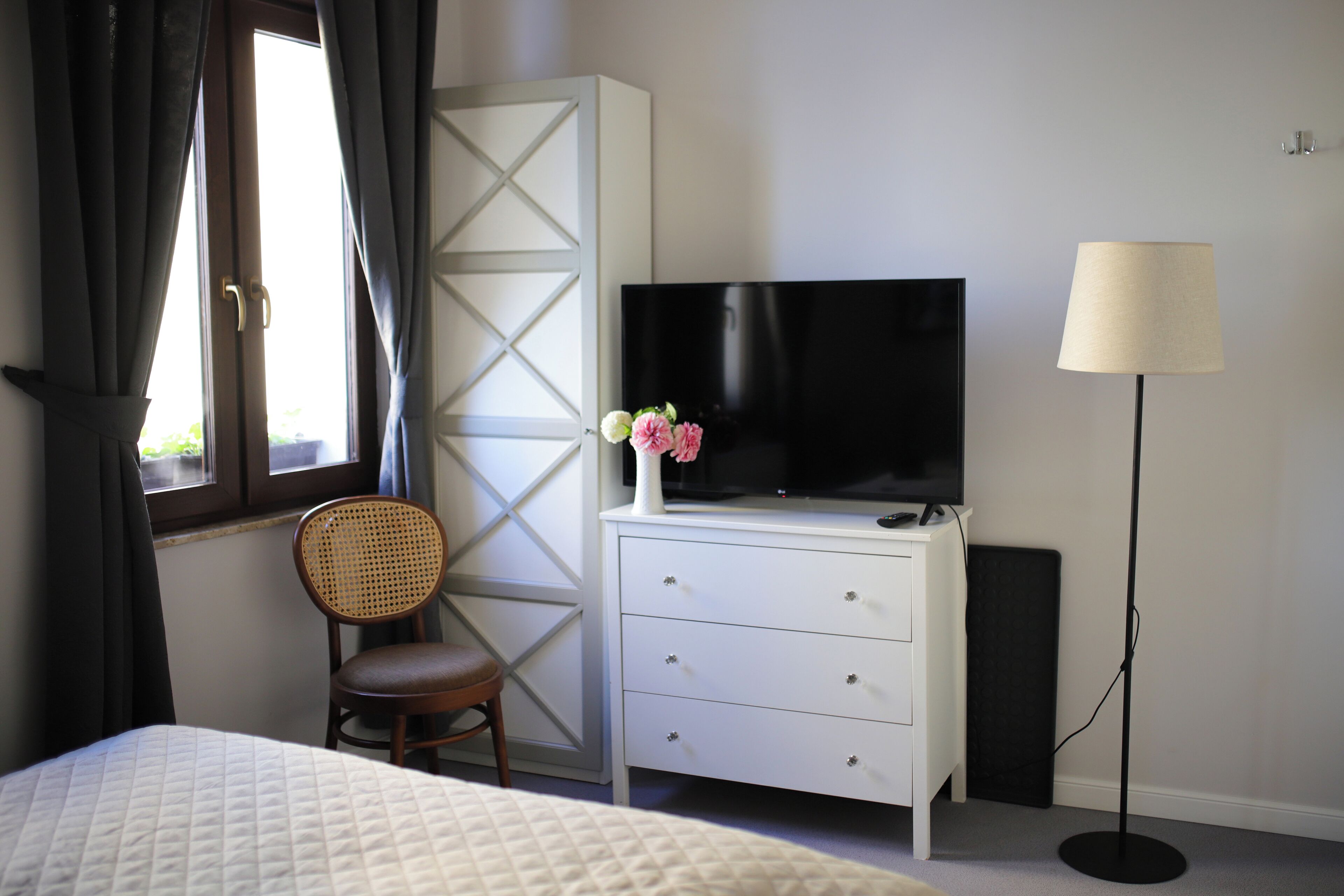 Quarto de hotel com uma cama, uma televisão em uma cômoda, uma cadeira e um abajur.