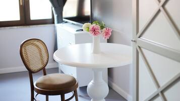 A room with a round white table, a wicker chair, a vase with flowers, a television, and a partially open door.