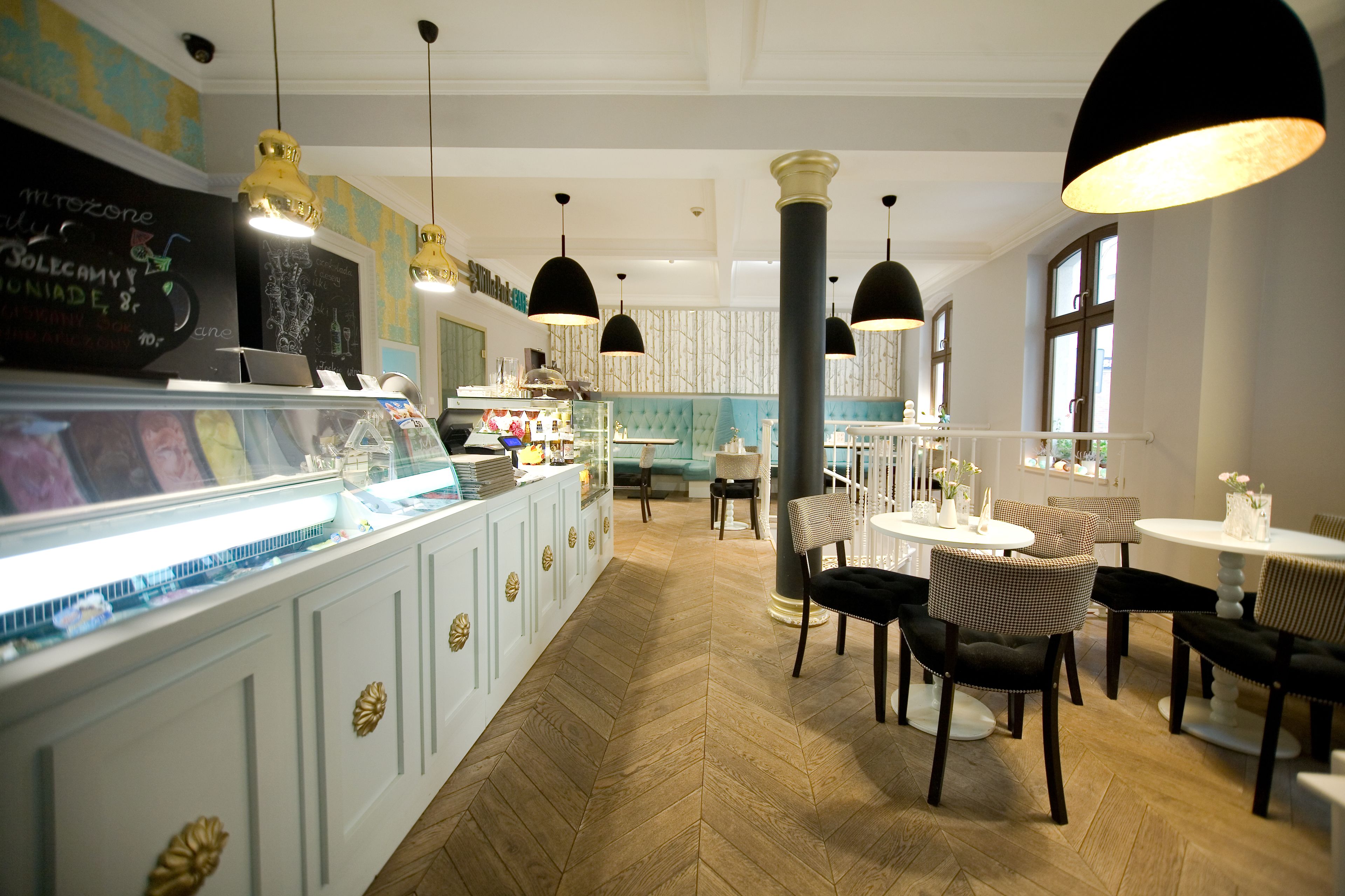 A restaurant interior with a herringbone wood floor, white cabinetry, and black pendant lighting.