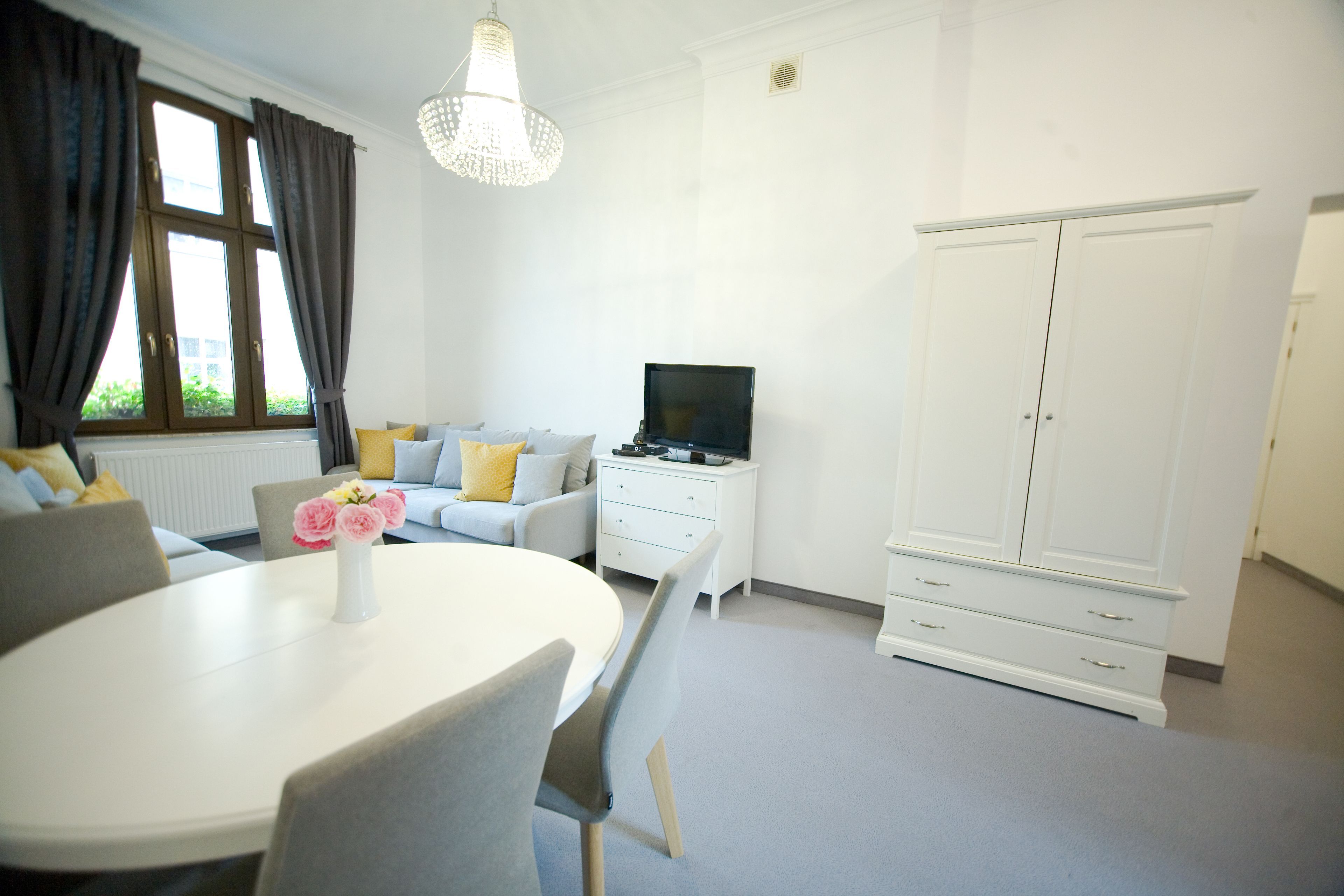 Una habitación moderna con una mesa redonda de comedor, un sofá con cojines, un televisor y un armario.