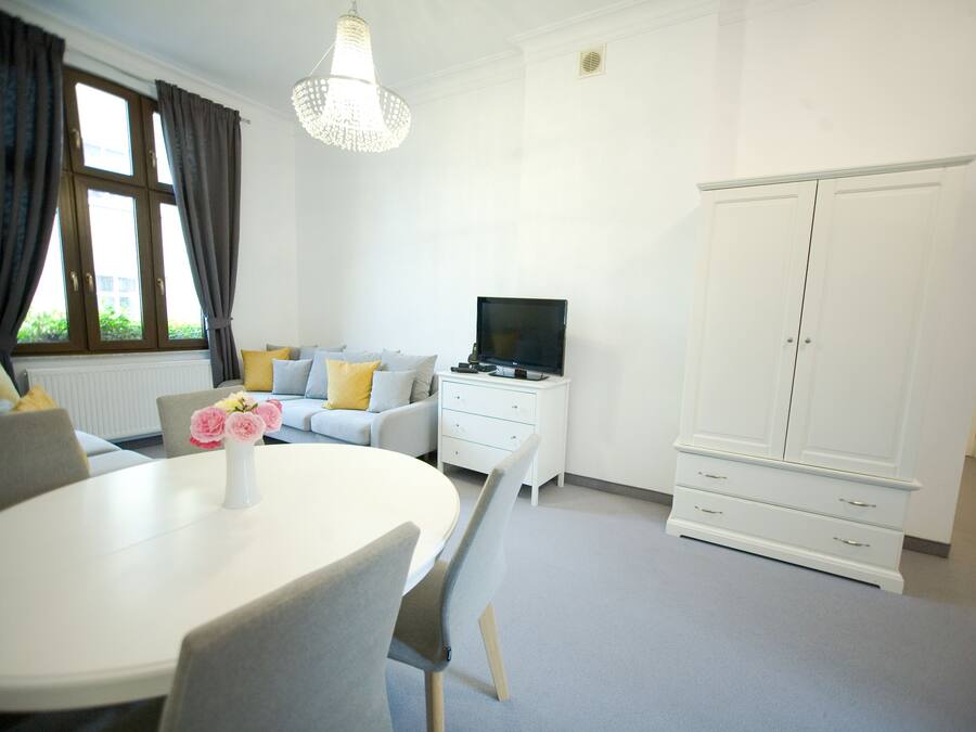 Una habitación moderna con una mesa redonda de comedor, un sofá con cojines, un televisor y un armario.