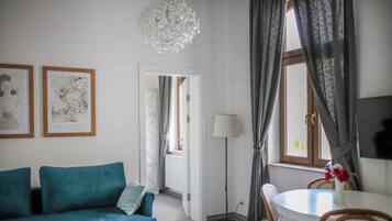 A room with a teal sofa, a round table with chairs, a floor lamp, and two framed artworks on the wall.