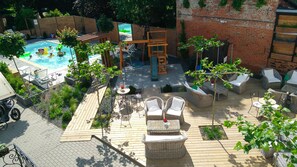 Uma área de piscina com deck de madeira, móveis de vime e parede de tijolos.