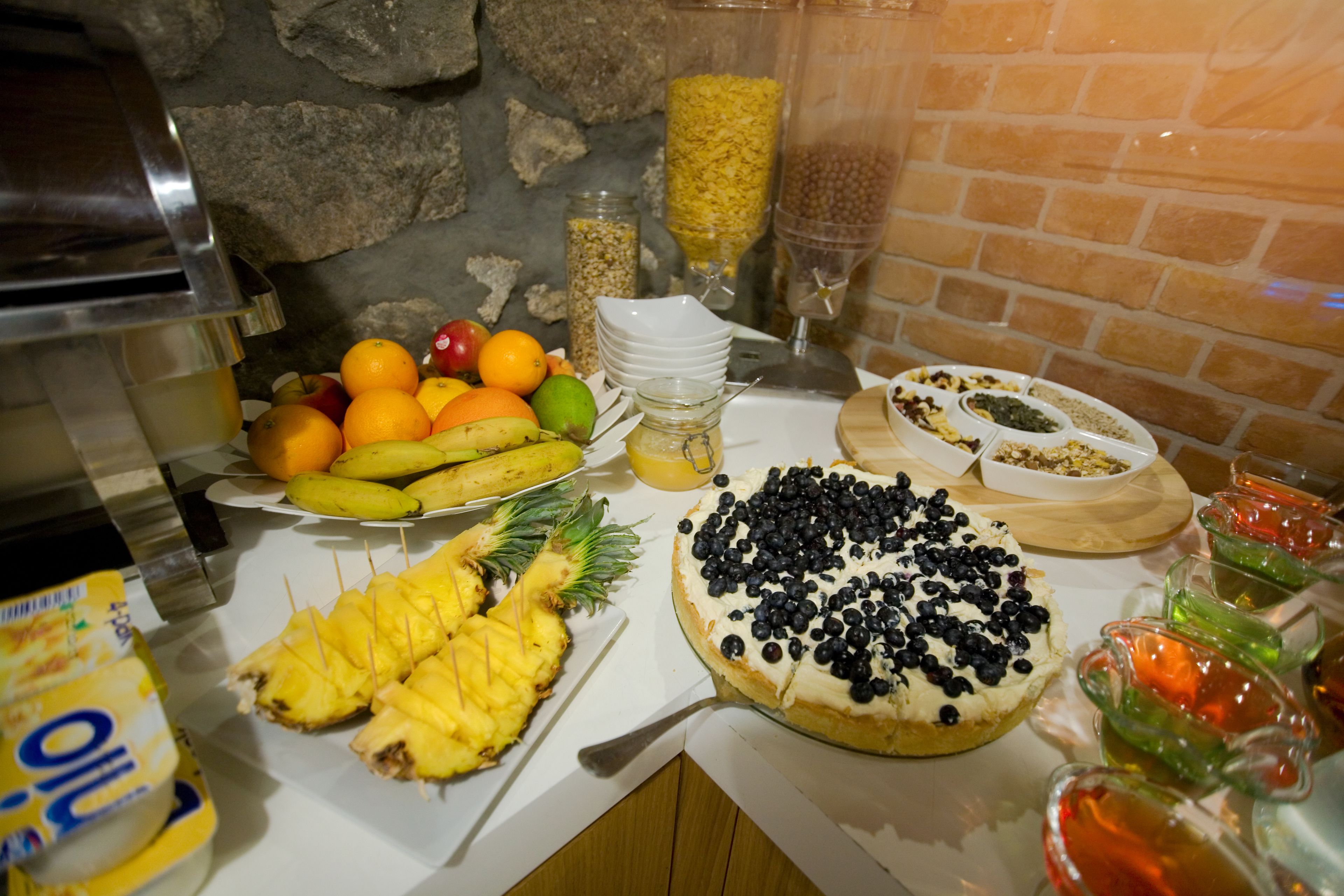 A buffet table with various fruits, a cake, and a juice dispenser.