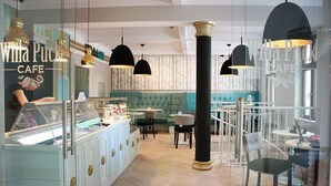 En café med en glasmontre, bløde siddepladser, hængende lamper og en synlig menutavle.