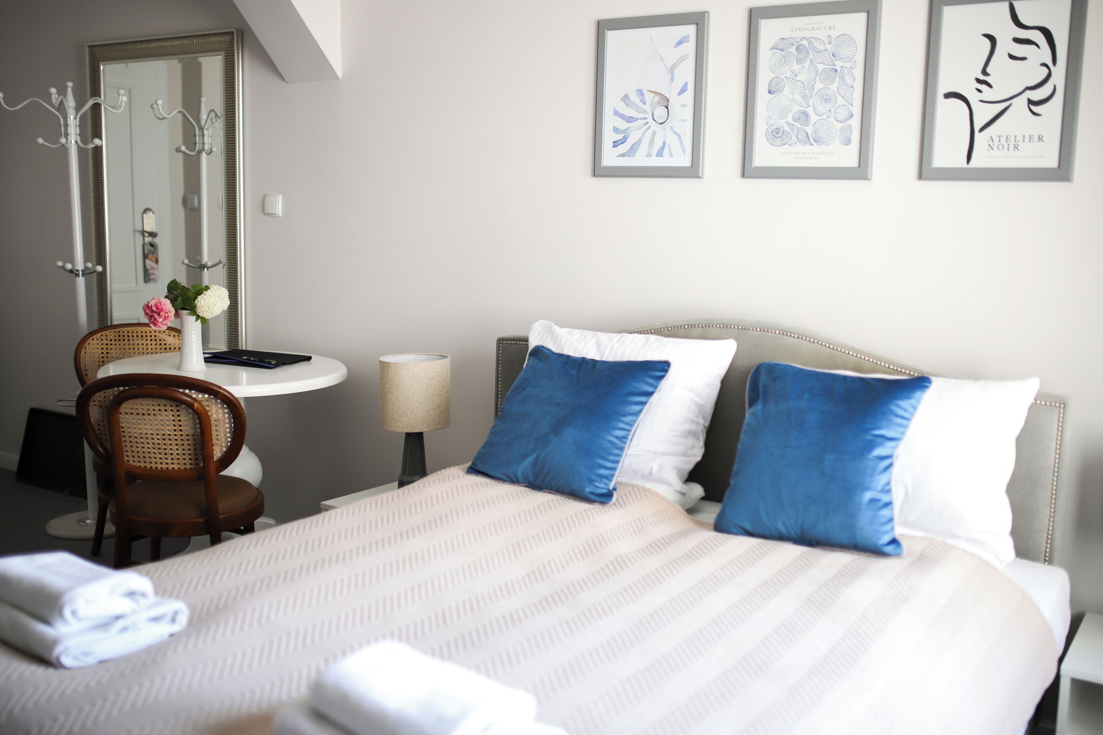 A neatly made bed with blue and white pillows, a chair, a lamp, and framed artwork on the wall.