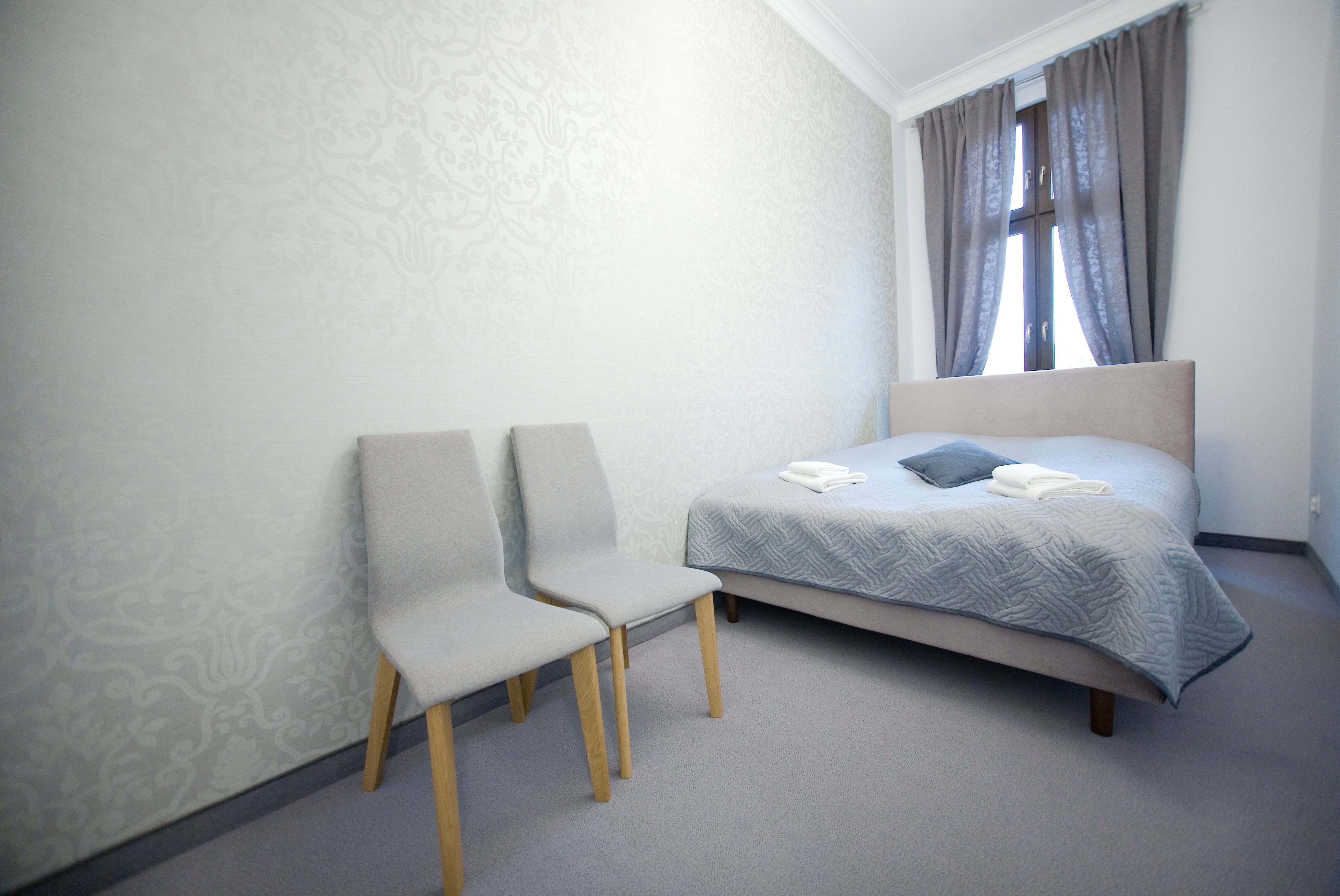 Een slaapkamer met een bed, twee stoelen en een raam met gordijnen.