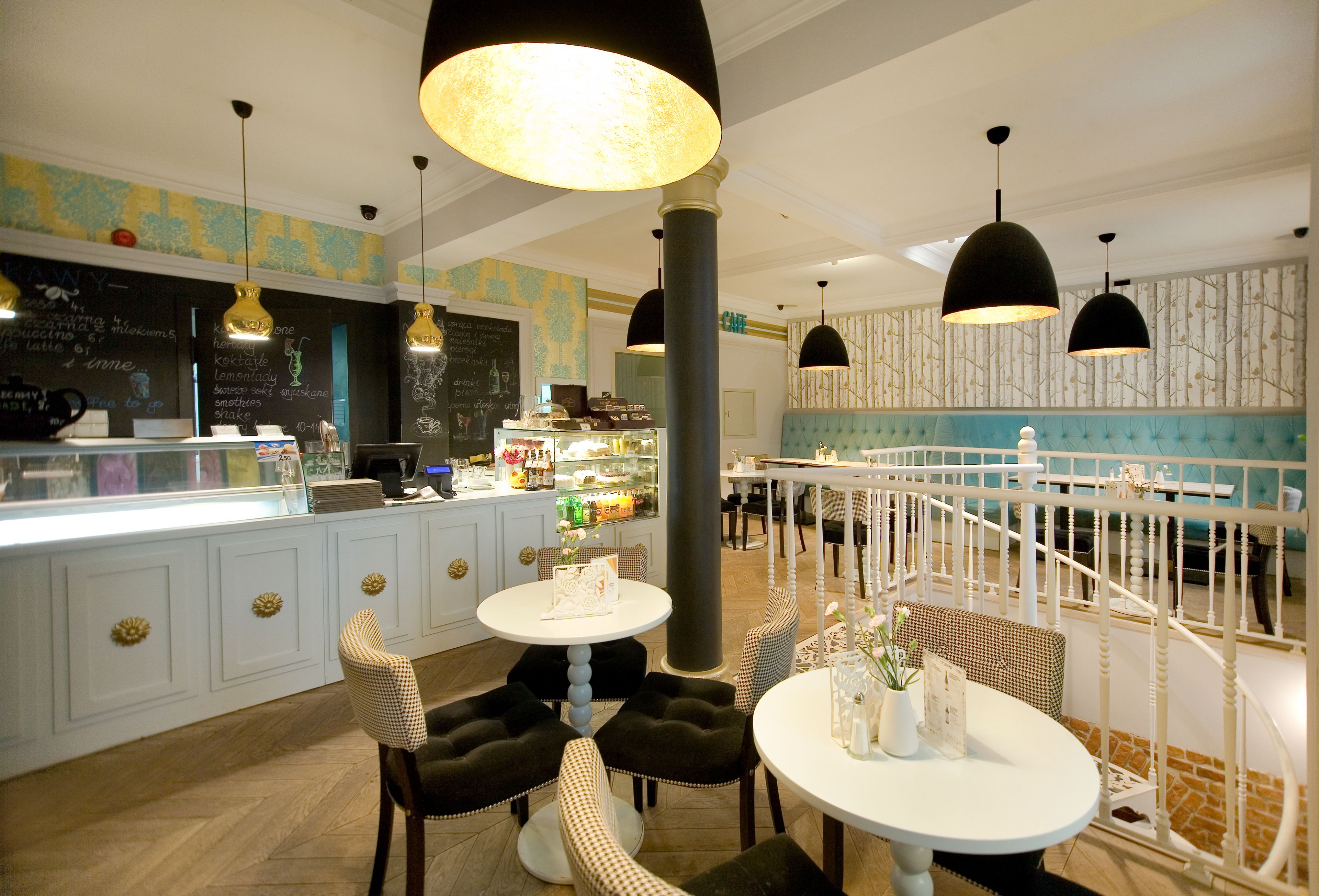 Un interior de restaurante con una zona de bar, sillas a cuadros, mesas redondas e iluminación colgante.
