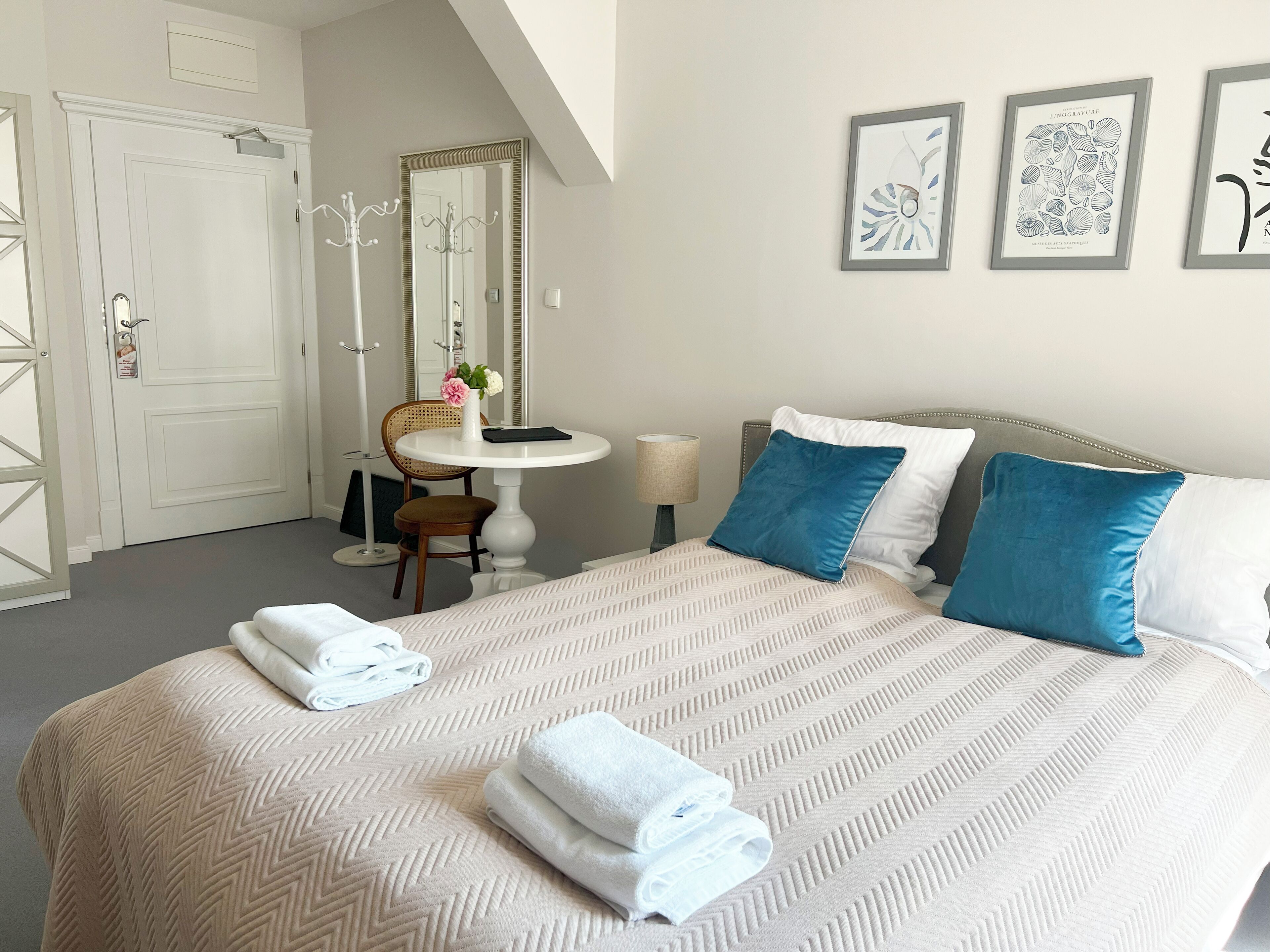 A neatly arranged bedroom with a large bed, two pillows, a bedside table with a lamp, and a chair.