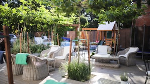 En udendørs terrasse med fletningsmøbler, et lille bord og plantekasser.