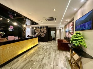A hotel reception area with a marble floor, a reception desk, a wall-mounted TV, and a decorative tree.
