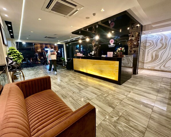 A hotel reception area with a reception desk, a sofa, and a potted plant.