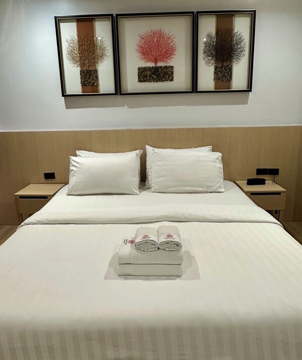 Une chambre d’hôtel avec un lit bien fait, deux tables de chevet et trois œuvres d’art encadrées accrochées au mur au-dessus du lit.