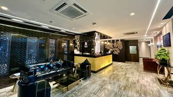 A modern hotel lobby with a reception desk, leather seating area, and a decorative wall.