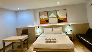 A hotel room with a bed, a desk, a chair, a sofa, and three paintings on the wall. - Sakura Sky Residence (Bangkok)