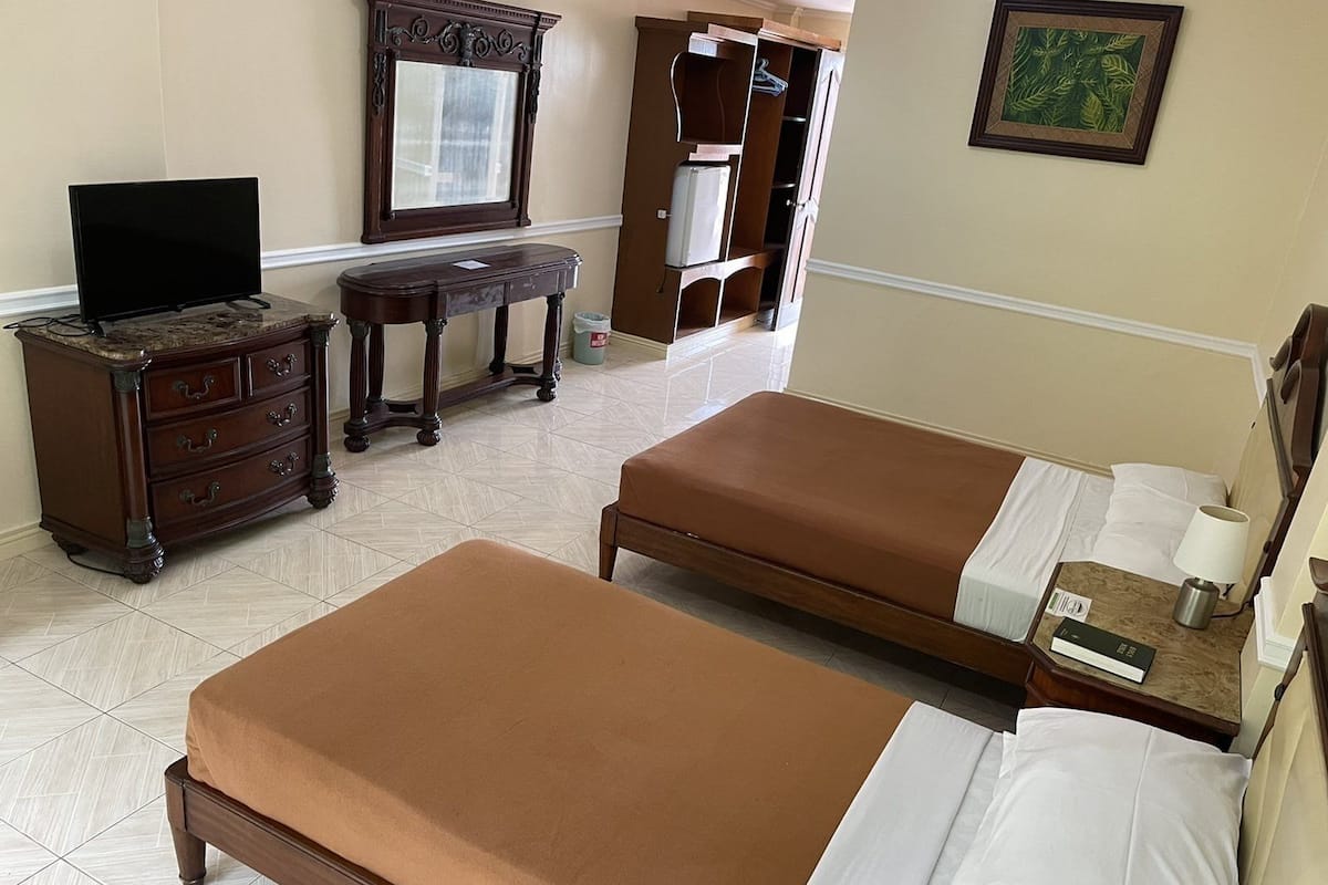 A hotel room with two beds, a dresser, a television, a desk, and a wardrobe.