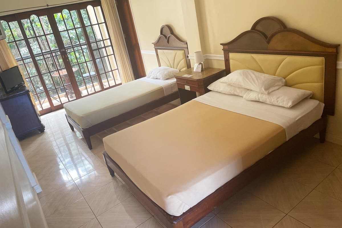 A hotel room with two beds, a wooden headboard, a small table with a lamp, and a TV on a cabinet.