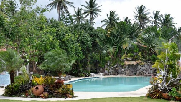A swimming pool surrounded by tropical vegetation and a stone wall. - Camiguin Highland Resort (Mambajao)