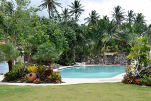 A swimming pool surrounded by tropical vegetation and a stone wall. - Camiguin Highland Resort (Mambajao)