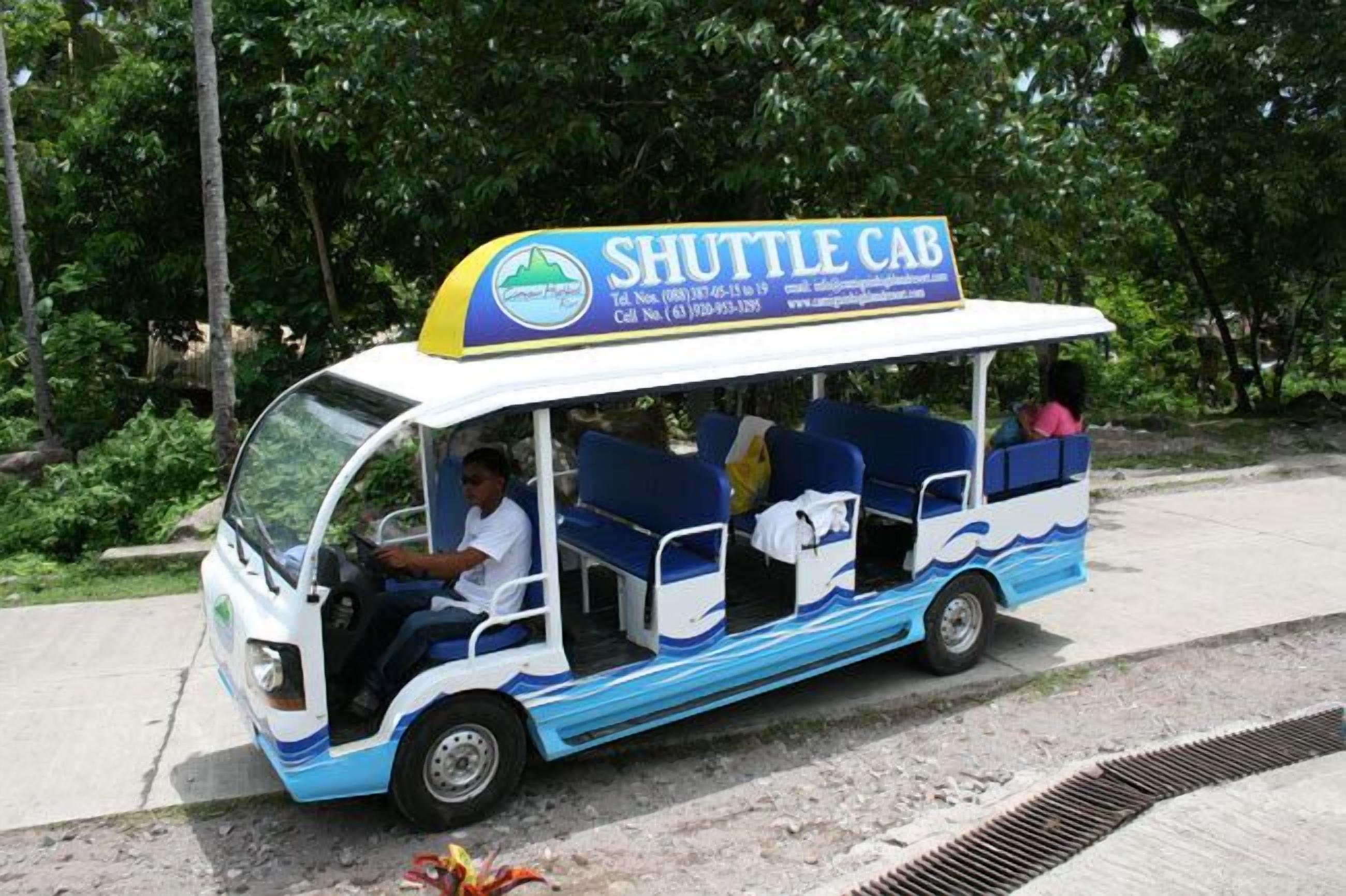 A shuttle cab with a blue and white design, labeled "SHUTTLE CAB," and a contact number on the top.