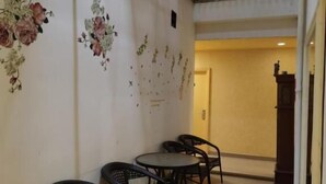 Ein Korridor mit einer Reihe schwarzer Korbstühle, einem kleinen runden Tisch, einer Wand mit floralen Verzierungen und einer Treppe mit Metallgeländer.