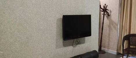 A living room with a black leather sofa, a flat-screen TV mounted on the wall, and a floor lamp.
