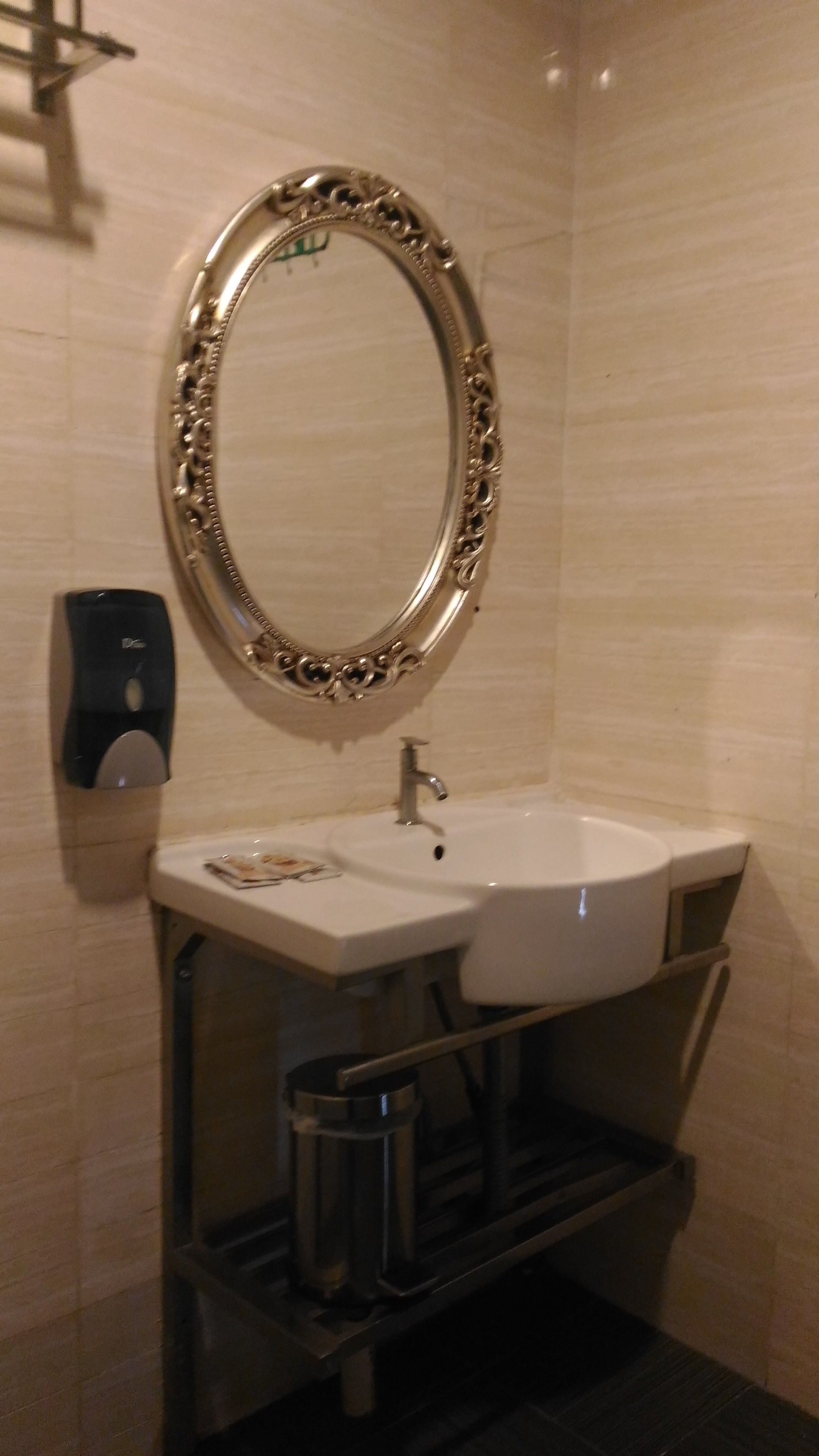 A bathroom with a large ornate mirror, a white sink, and a soap dispenser.