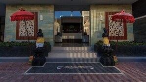 A hotel entrance with two statues, a red umbrella, and a decorative wall. - RaBaSTa Mahayana Kuta (Kuta)