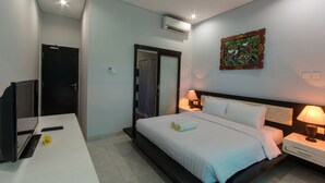A hotel room with a bed, bedside tables, a desk with a computer, and an air conditioning unit. - RaBaSTa Mahayana Kuta (Kuta)