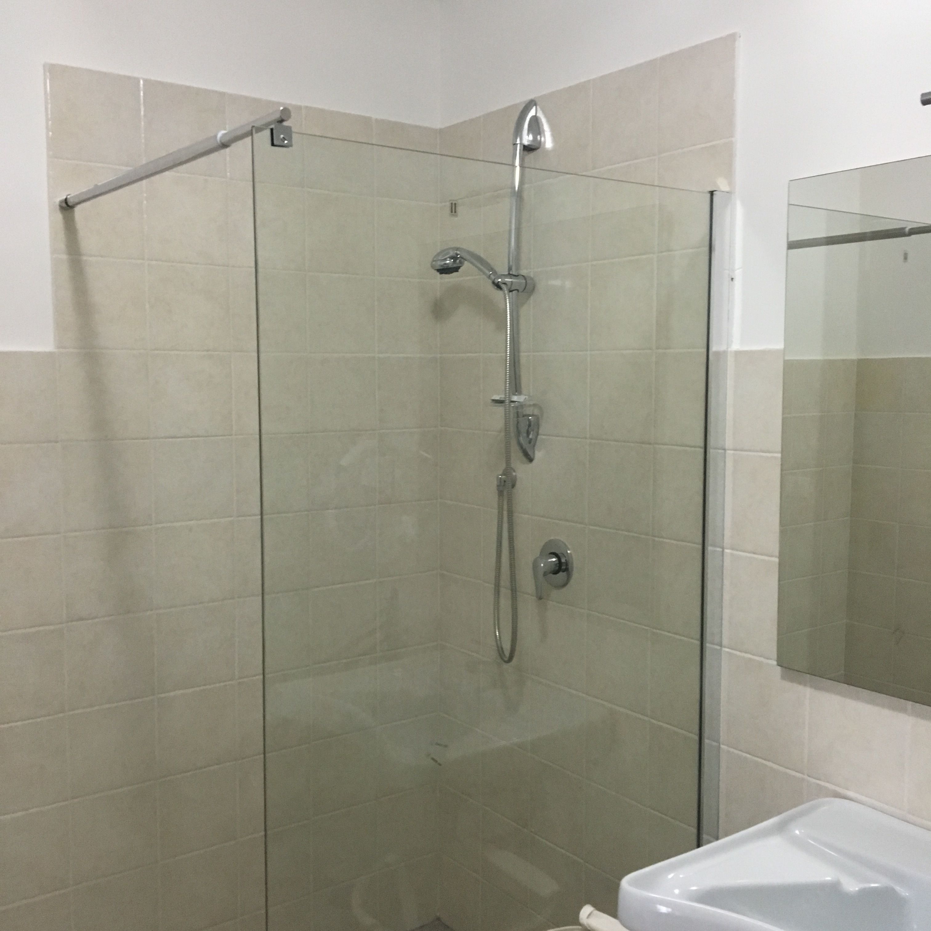 Cabina de ducha con paredes de vidrio, cabezal de ducha de mano y llave de pared.