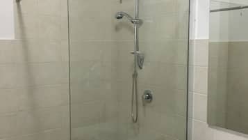 Cabina de ducha con paredes de vidrio, cabezal de ducha de mano y llave de pared.