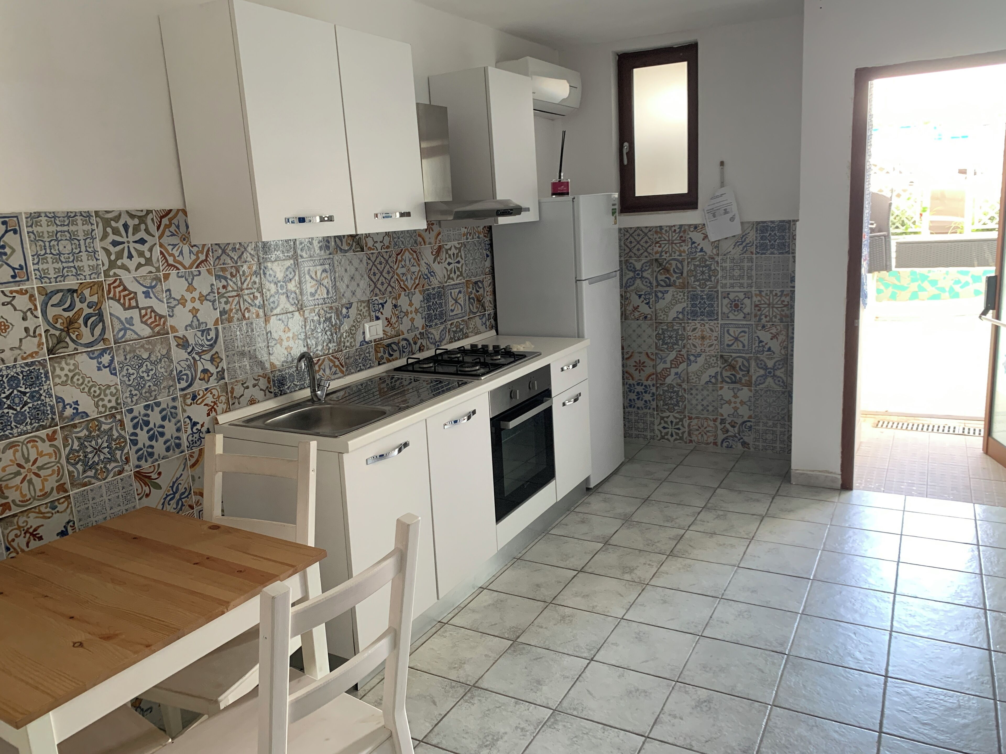 Una cucina compatta con mobili bianchi, un piano cottura a gas, un lavello e uno schienale piastrellato.