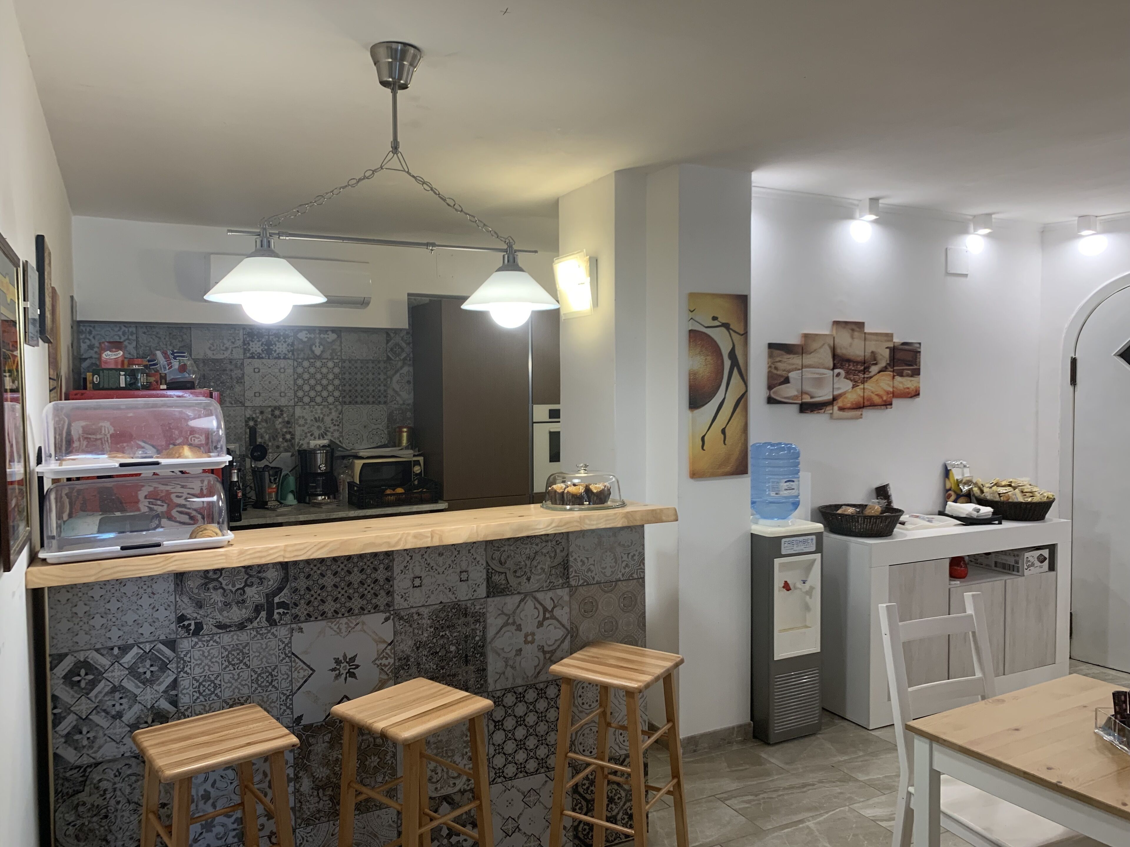A modern kitchen with a wooden countertop, three stools, a water dispenser, and a coffee machine.