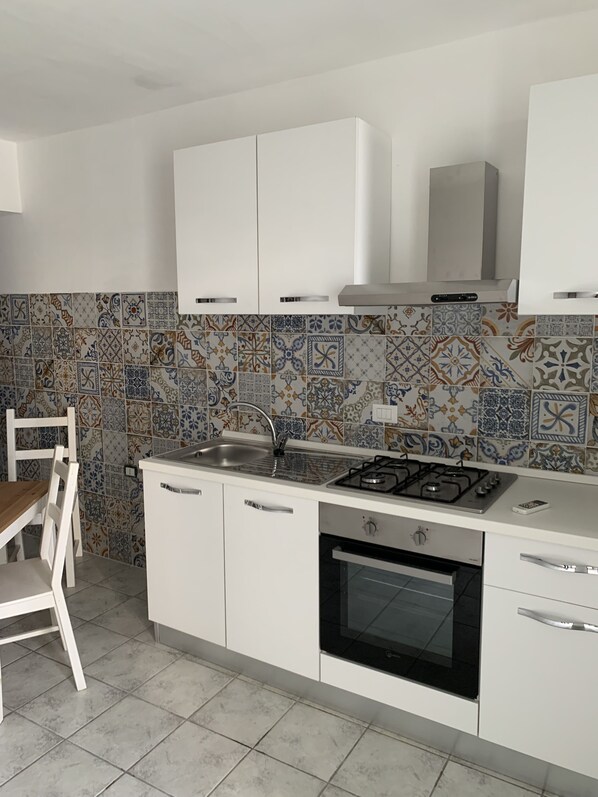 A kitchen with white cabinets, a gas stove, a sink, and a tiled backsplash.