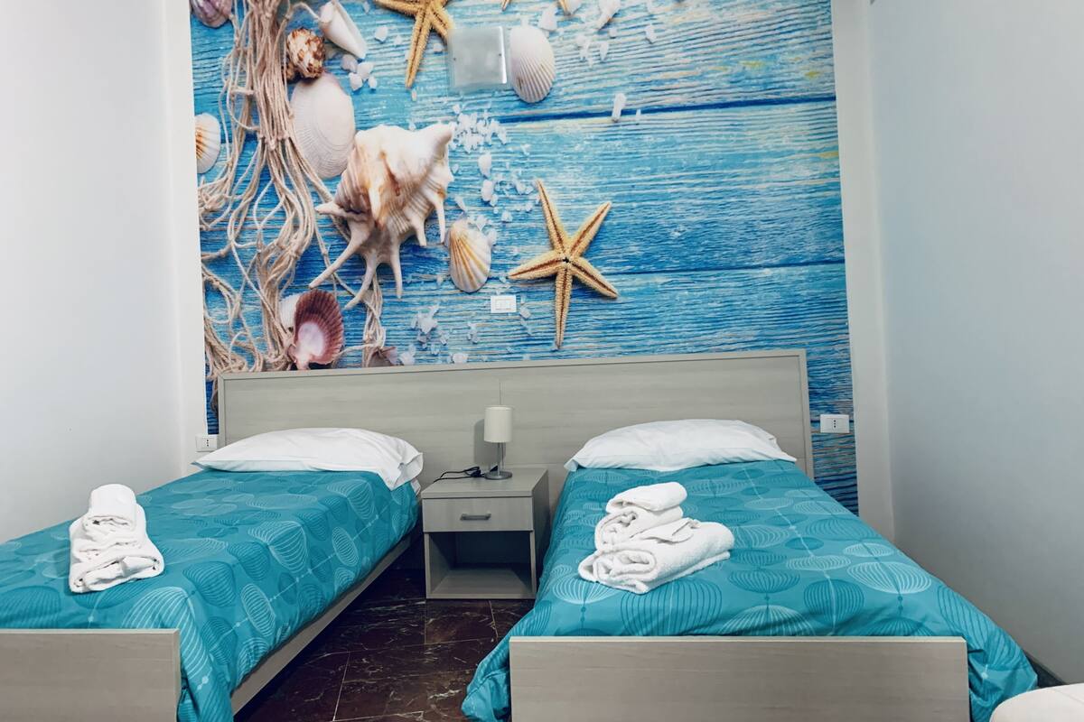 A hotel room with two beds, a nightstand, and a wall mural of seashells and starfish.