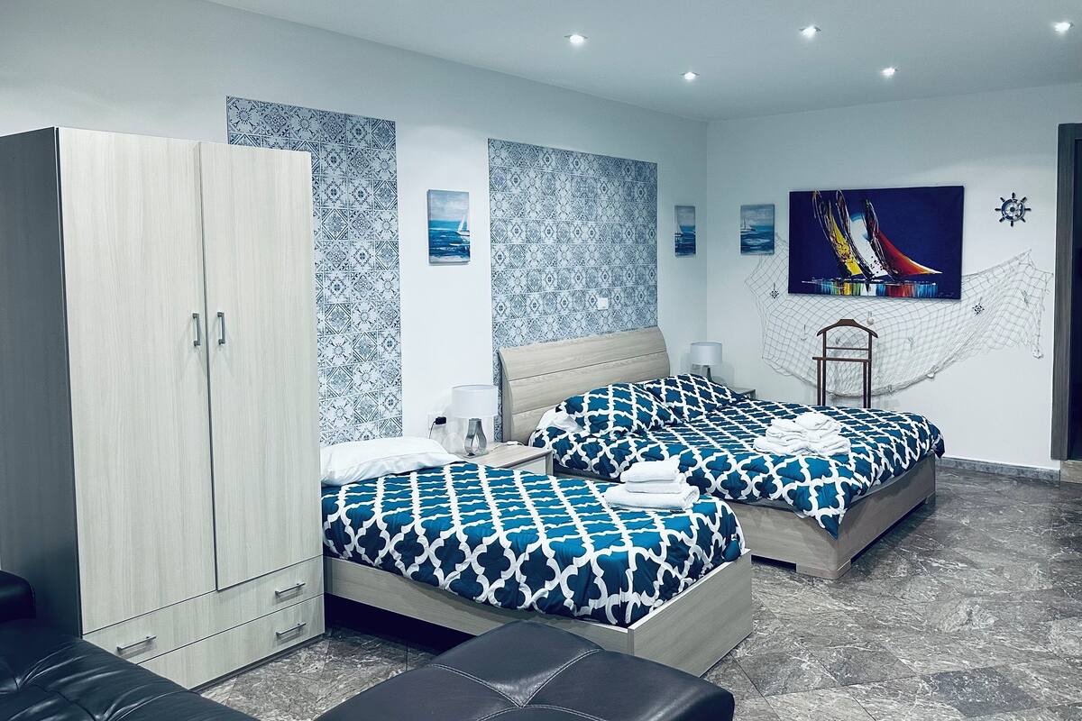 A modern bedroom with two beds, a wardrobe, and a decorative wall with nautical-themed artwork.
