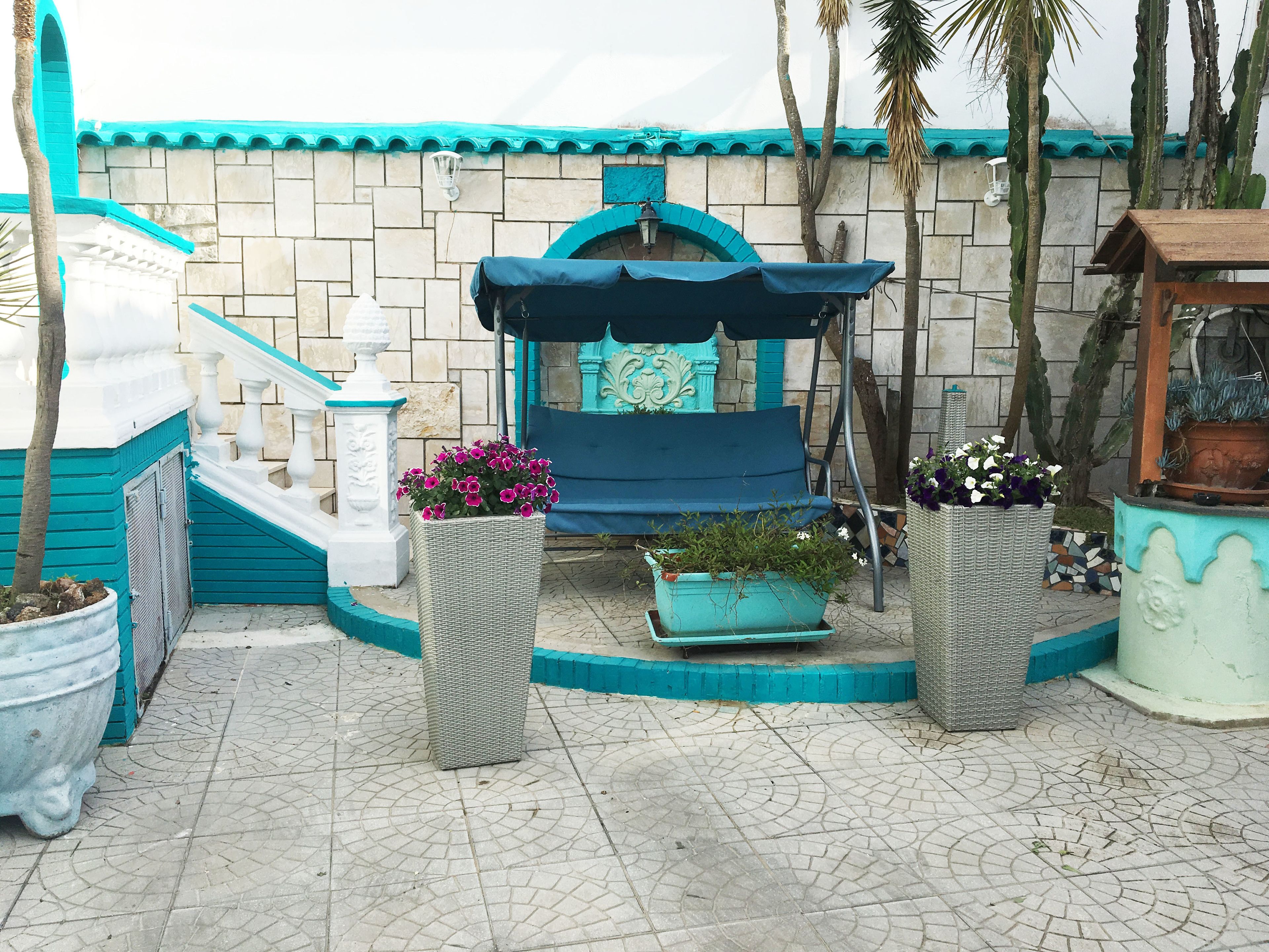 Eine Terrasse mit einer blauen Bank, Kübelpflanzen und einem gefliesten Boden.