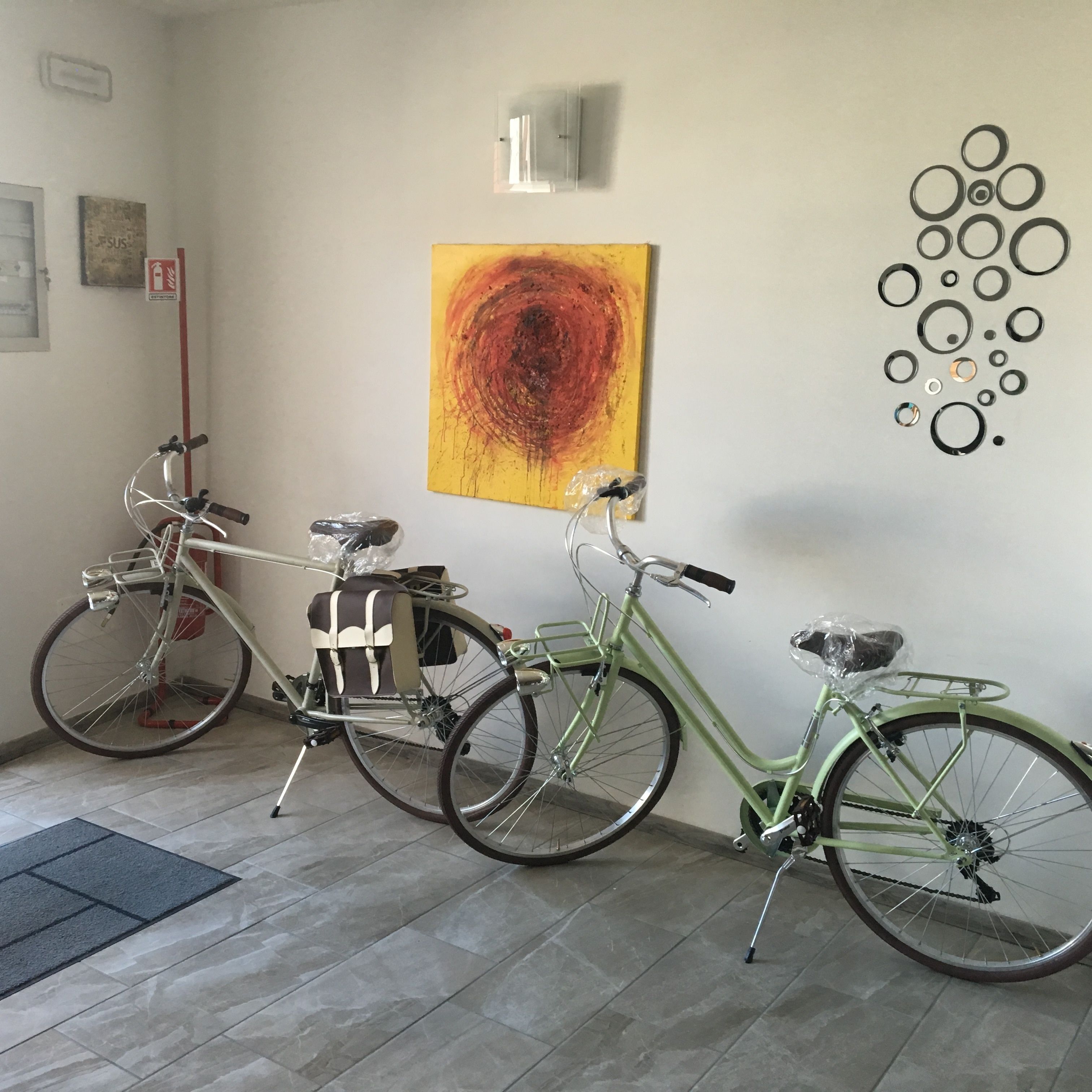 Two bicycles parked indoors, a wall-mounted abstract painting, and a wall decoration of circles.