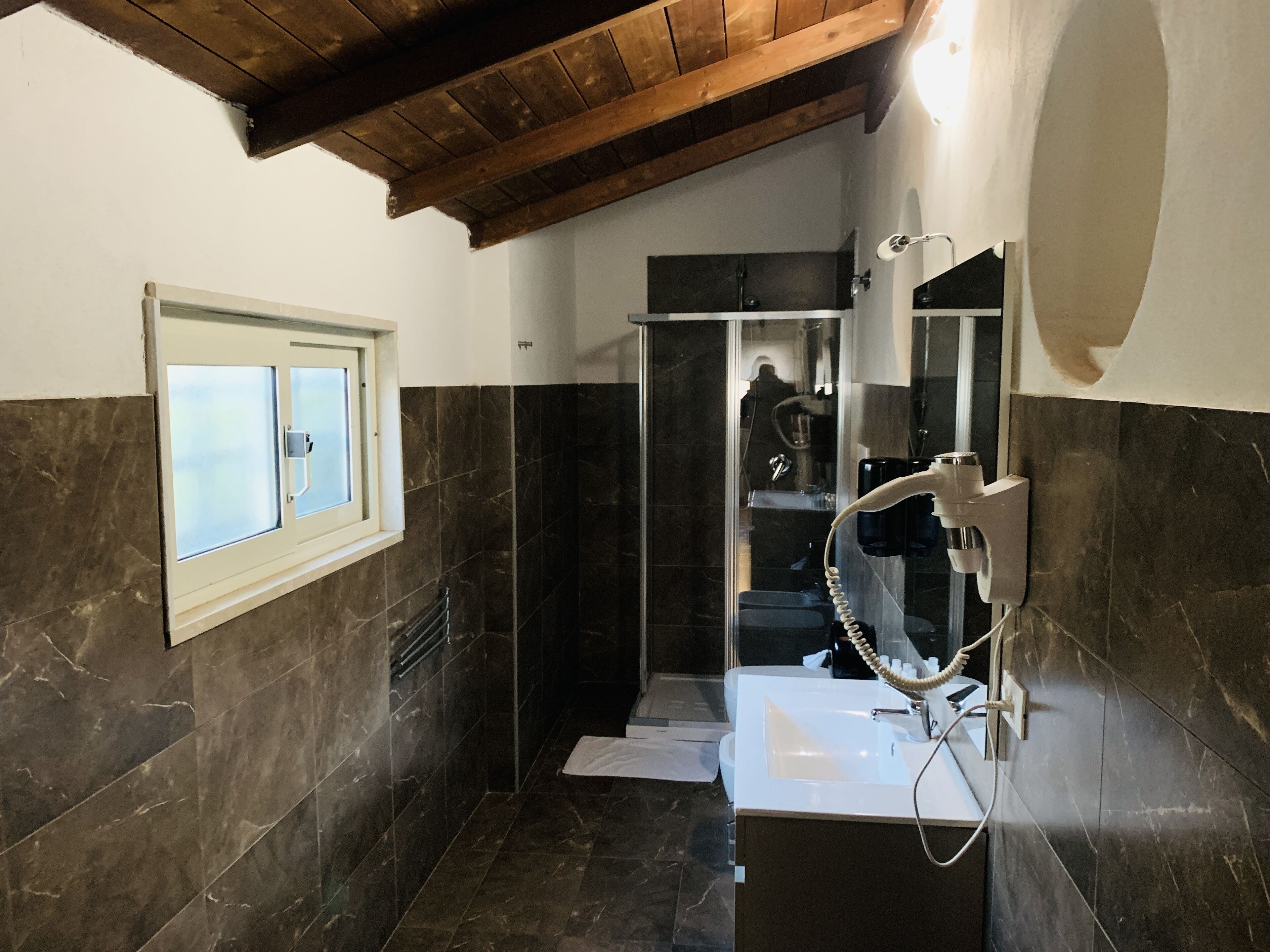 A bathroom with dark marble walls, a wooden ceiling, a white sink, and a glass shower enclosure.