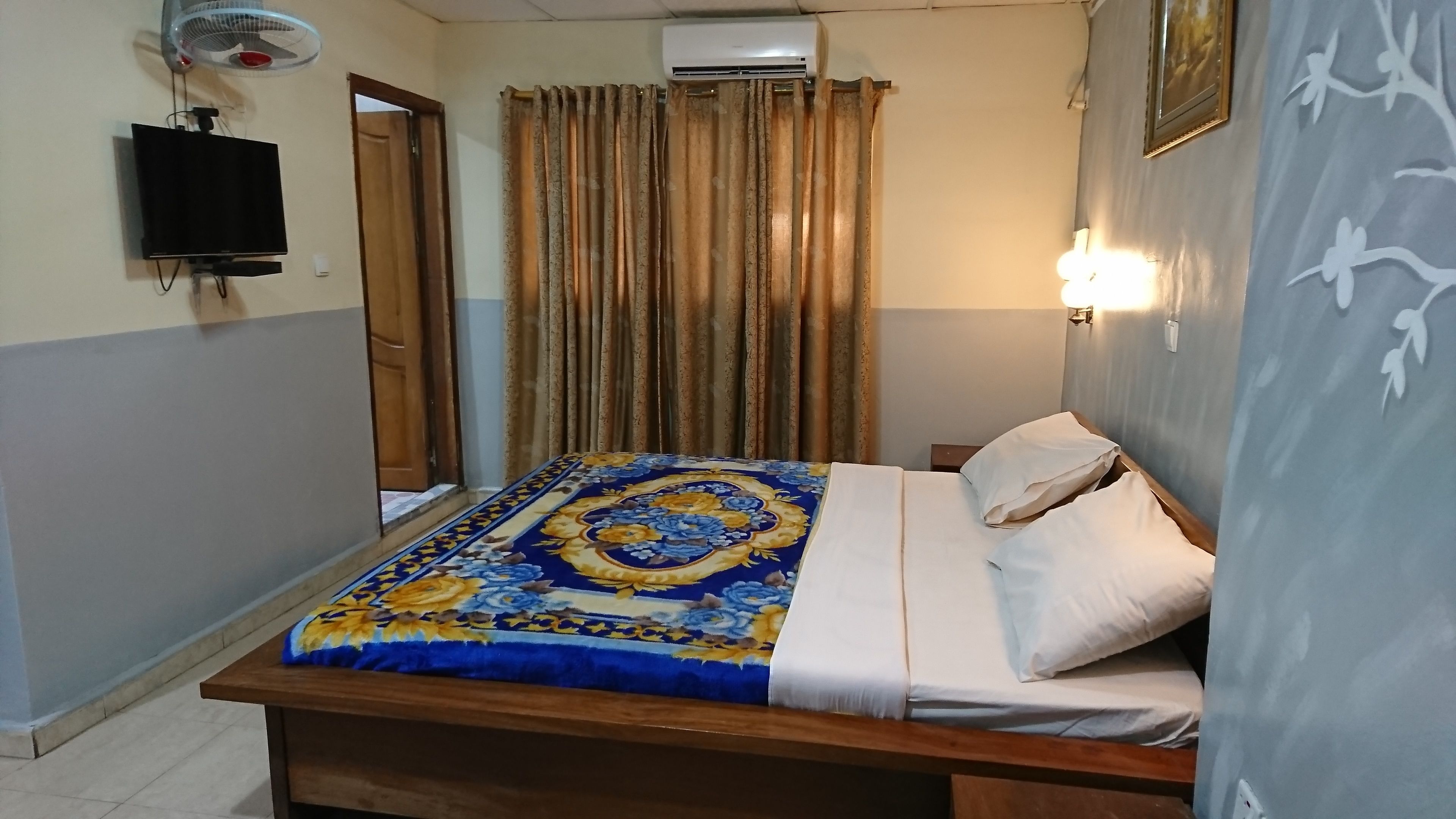 Quarto com cama, cortinas, TV fixada na parede e ar condicionado.