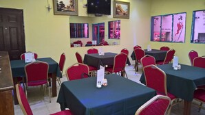 A dining area with tables and chairs, a television mounted on the wall, and framed pictures on the walls. - Hotel Pour Vous (Kinshasa)
