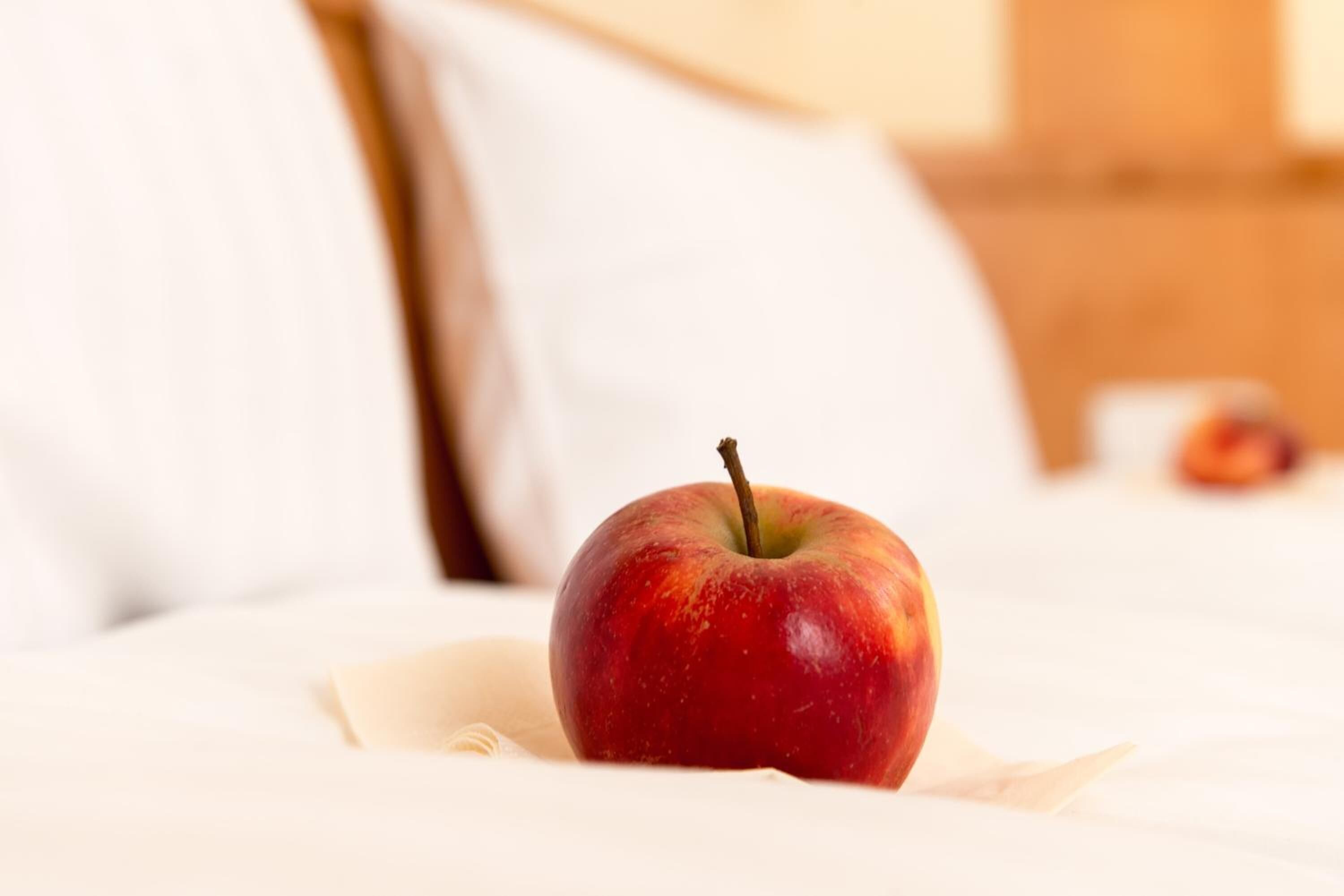 Una manzana sobre una cama con ropa de cama y almohadas blancas.