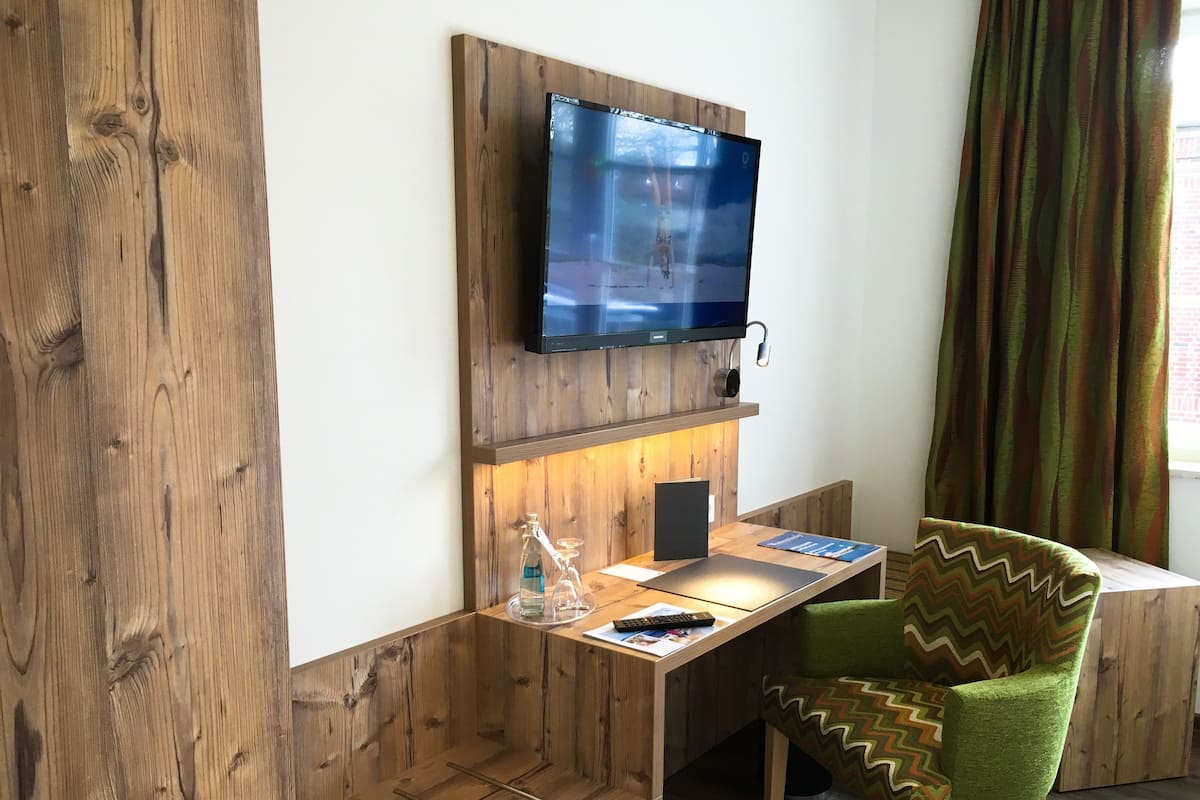Una habitación moderna con un escritorio de madera, un televisor montado y una silla verde.