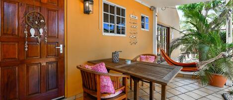 A wooden door with a welcome sign, a table with chairs, and a hammock.